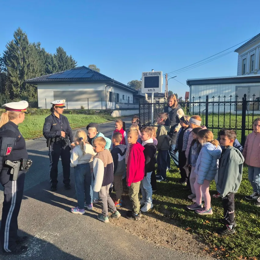 Eine Gruppe von Kindern steht auf dem Rasen vor einer Straße, wobei zwei Polizeibeamte am Straßenrand stehen.