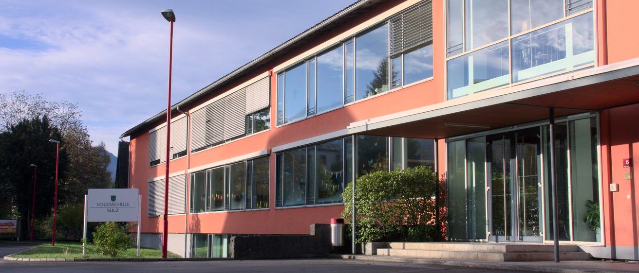 Ein orangefarbenes Gebäude mit Glasfenstern und einem Schild auf der linken Seite und einem roten Pfosten auf der linken Seite.
