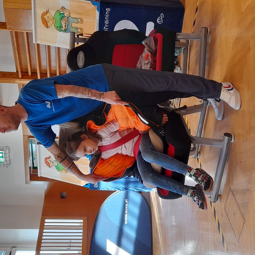 Ein Mann justiert den Sicherheitsgurt eines kleinen Mädchens, das auf einem Trainingsstuhl in einem Fitnessstudio sitzt.