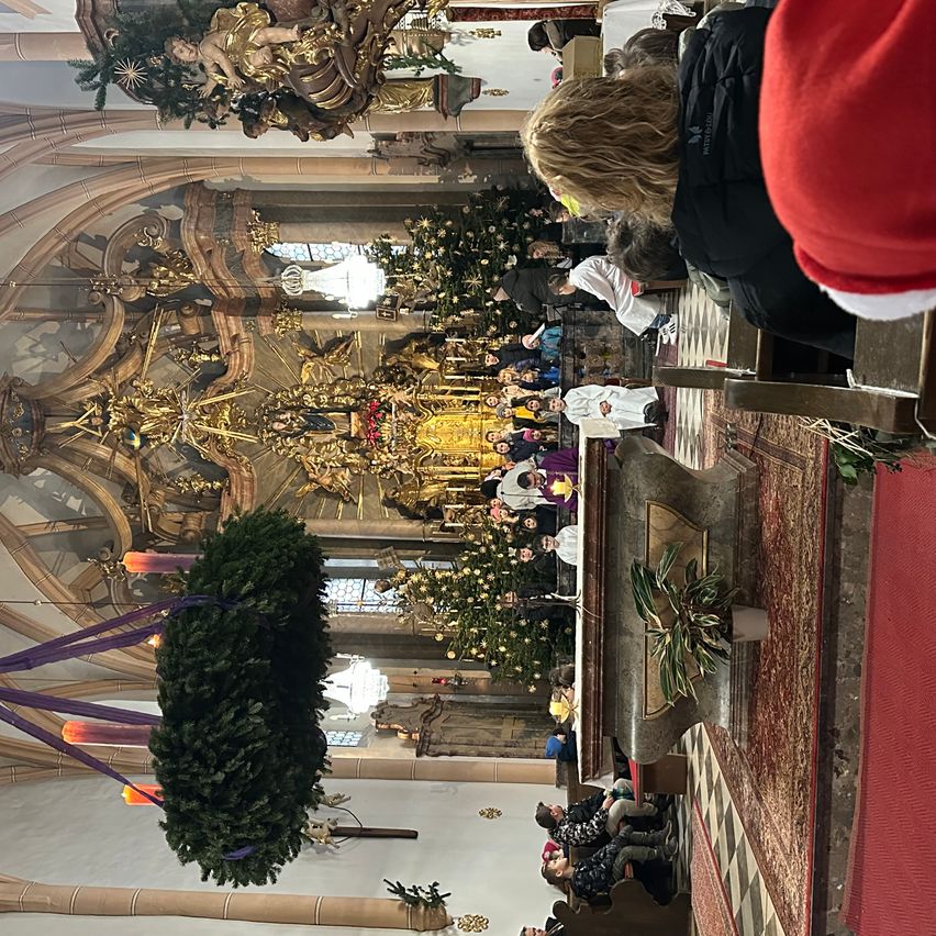 Ein weihnachtlicher Kirchengottesdienst mit Menschen in traditionellen weißen Gewändern und goldenen Ornamenten. Der Altar ist mit einem großen Kranz und Kerzen geschmückt. Der Blick ist von oben und zeigt den gesamten Raum.