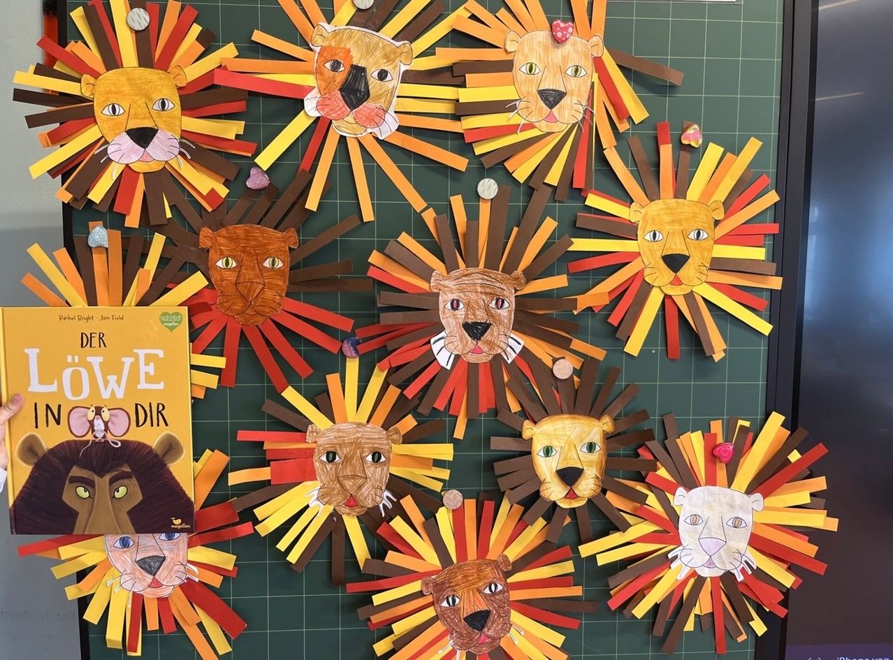 Eine Sammlung von Papierlöwenkopf-Basteleien, die in einem Kreis auf einem grünen Hintergrund angeordnet sind. Jeder Löwenkopf hat unterschiedliche Gesichtszüge und ist von mehrfarbigen Papierstreifen umgeben.