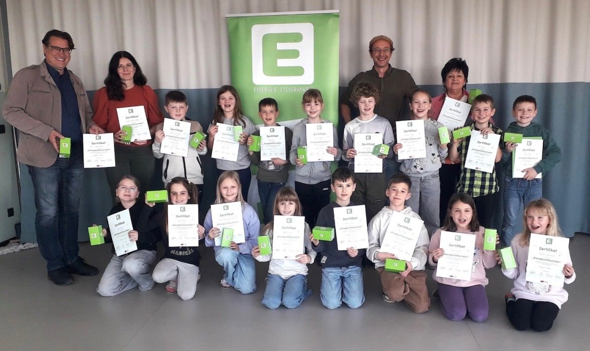Gruppenfoto von Kindern, die Zertifikate halten und vor einem grünen Banner mit Text und Logos lächeln.