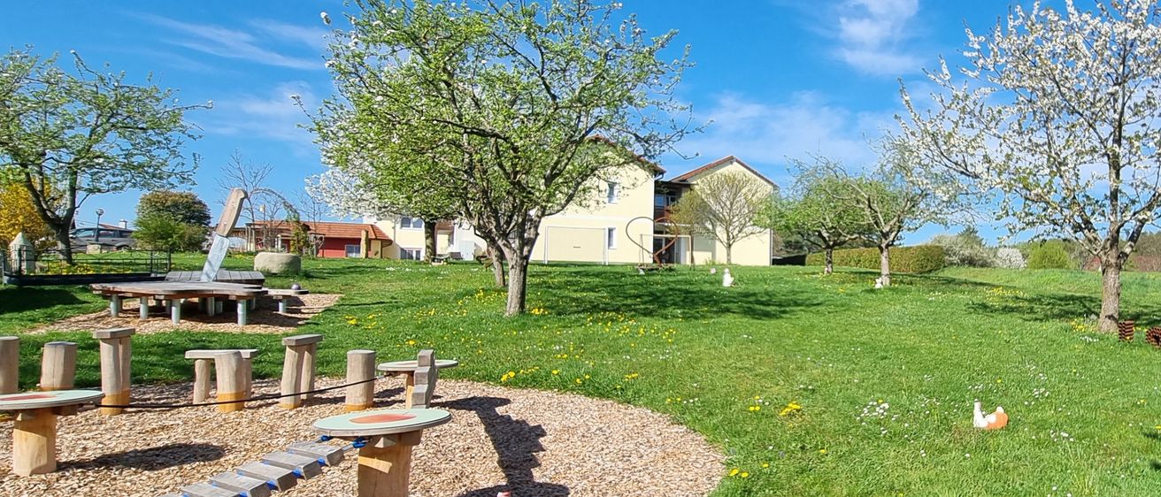 Outdoor-Spielplatz mit gelbem Gras und blühenden Apfelbäumen an einem sonnigen Tag.
