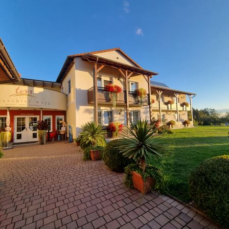 Der Eingang des Buschler-Mogge Hotels mit einem gepflasterten Weg, Topfpflanzen und einem roten Blumenbalkon an einem sonnigen Tag.