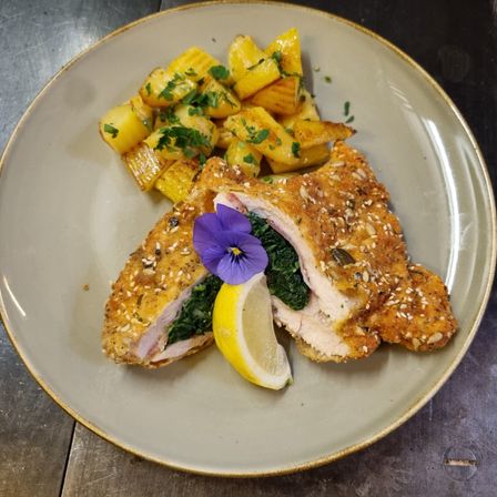 Ein Teller mit einer gebratenen Hähnchenbrust, begleitet von einer Beilage aus Kartoffelpüree und einer Zitronenscheibe, garniert mit einer lila Blume.