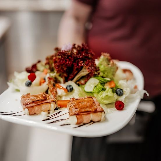 Ein weißer Teller mit Salat und zwei Scheiben Prosciutto mit einer Saucenüberzug.