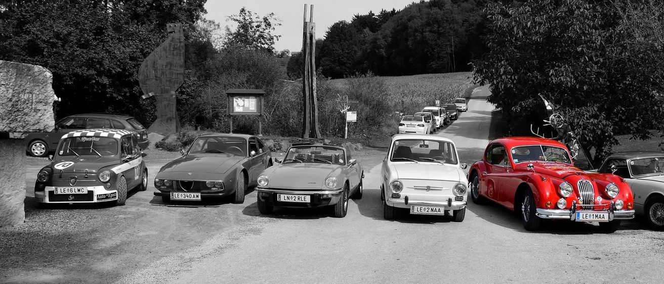 Ein Schwarz-Weiß-Foto von Oldtimern, die am Straßenrand geparkt sind, mit einer Person, die in einem der Autos sitzt.