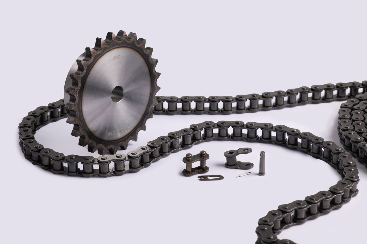 Nahaufnahme eines Kettenrads und einer Kette. Das Kettenrad hat einen Metallring mit Zähnen und einem zentralen Loch. Die Kette besteht aus Gliedern, die durch Nieten verbunden sind.