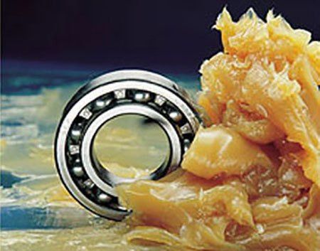 Eine Nahaufnahme eines Kugellagers mit einer dicken, viskosen Substanz darum herum, möglicherweise Schmiermittel. Das Lager ist metallisch und scheint in der Substanz eingetaucht zu sein.