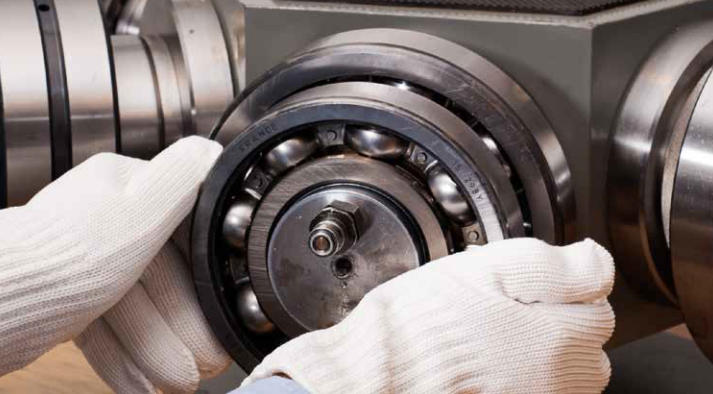 A person wearing white gloves is working on a machine, possibly inspecting or repairing a part. The machine has metal components and the person is holding a circular metal piece.
