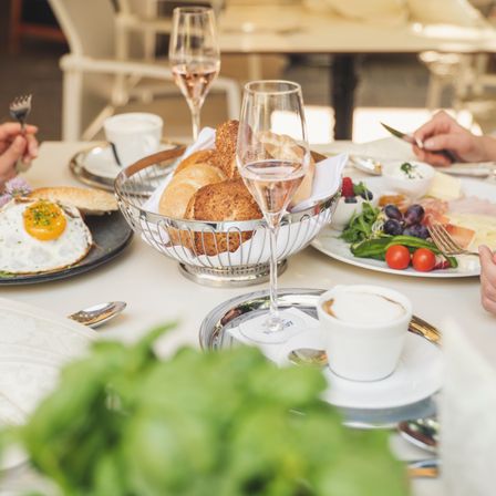 Ein Frühstückstisch mit Brot, Eiern und verschiedenen Frühstücksartikeln, zusammen mit Weingläsern, Besteck und einem Teller mit Salat.