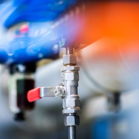 Ein Nahaufnahme eines Edelstahlventils mit rotem Griff und einem blauen Rohr im Hintergrund.