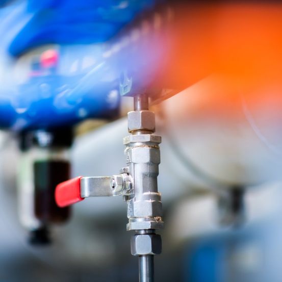 Ein Nahaufnahme eines Edelstahlventils mit rotem Griff und einem blauen Rohr im Hintergrund.