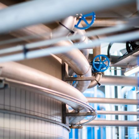 Eine industrielle Anlage mit verschiedenen Metallrohren, Ventilen und Geräten. Die Rohre sind mit blauen Ventilen verbunden und von Metallstrukturen gestützt.