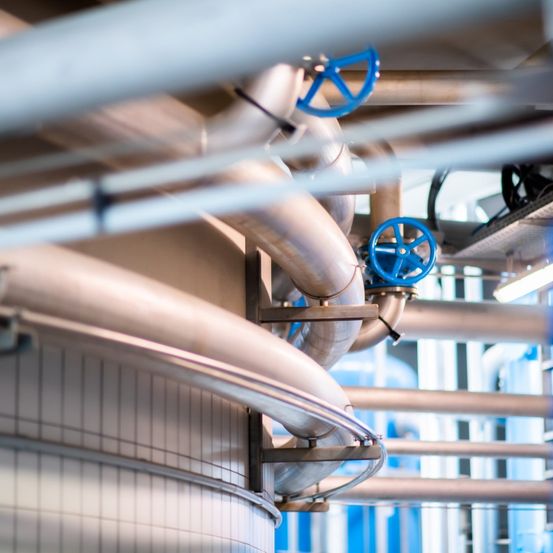 Eine industrielle Anlage mit verschiedenen Metallrohren, Ventilen und Geräten. Die Rohre sind mit blauen Ventilen verbunden und von Metallstrukturen gestützt.