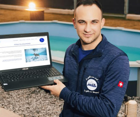 Ein Mann hält einen Laptop vor einem oberirdischen Pool, lächelt, mit einer Schwimm-Website auf dem Laptop-Bildschirm.