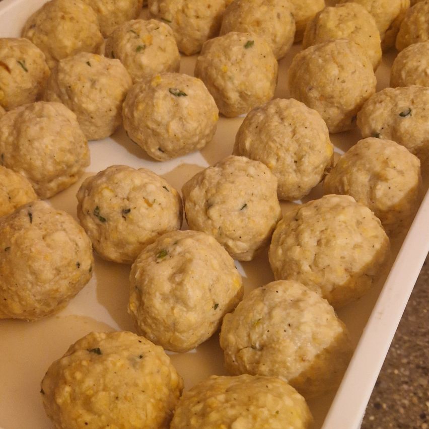 Ein Tablett mit goldenen, gewürzten Fleischbällchen mit einem Hauch von Kräutern, bereit zum Kochen.