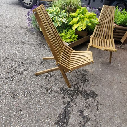 Zwei gefaltete Holzstühle stehen vor einem Garten mit Lavendel und grünen Pflanzen.