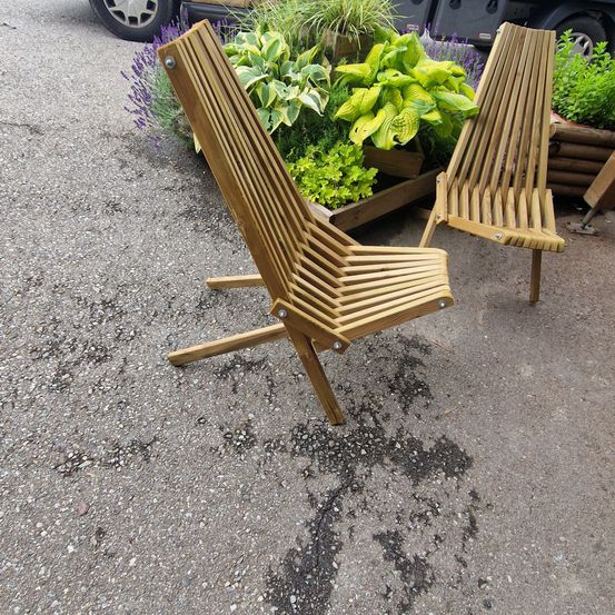Zwei gefaltete Holzstühle stehen vor einem Garten mit Lavendel und grünen Pflanzen.