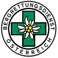 Rundes Logo für Bergrettungsdienst Österreich mit grünem Kreuz und Blume in der Mitte.