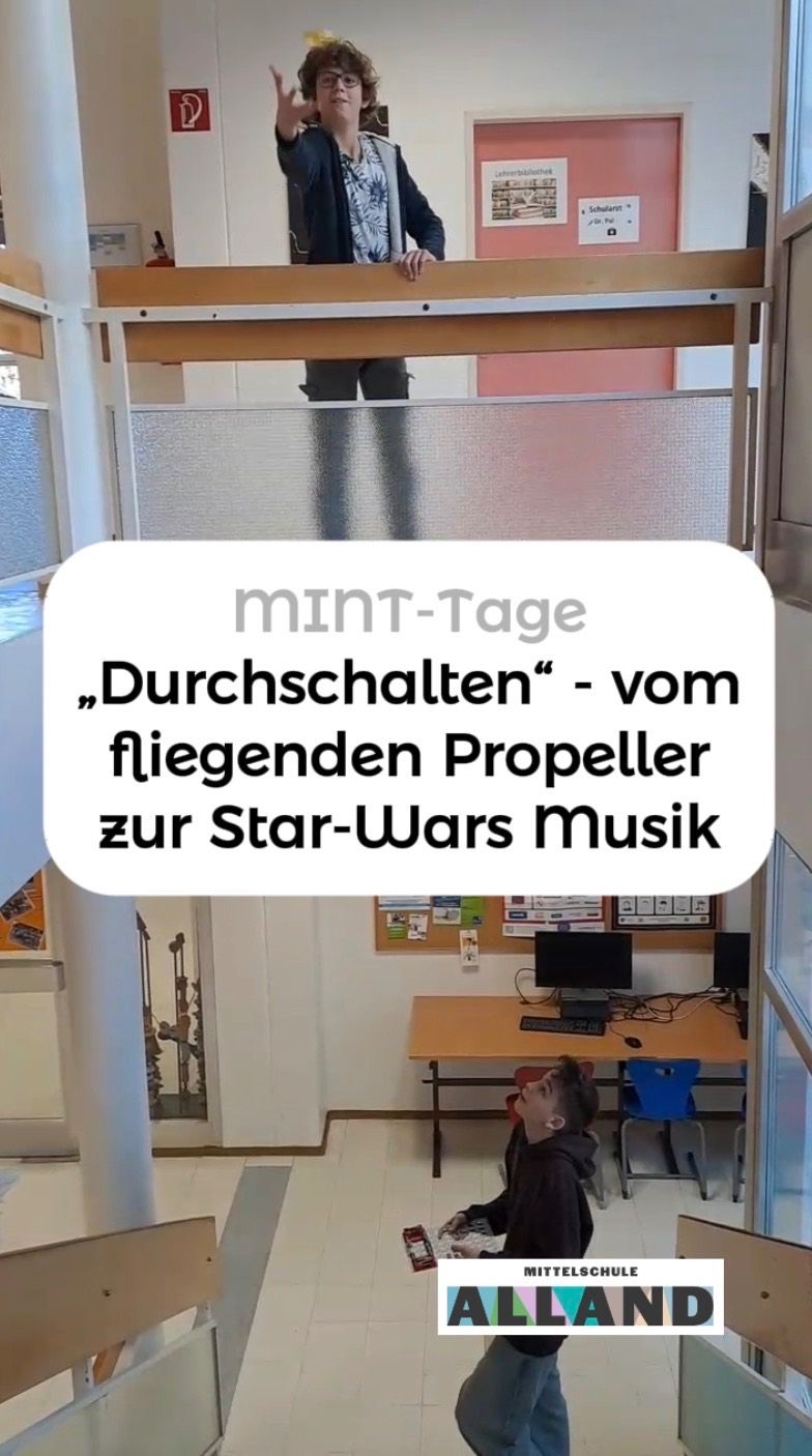 A person is standing near a glass partition, likely in an office. The text overlay reads 'MINT-Tage Durchschalten vom fliegenden Propeller zur Star-Wars Musik.' A desk with a computer and keyboard is visible in the background.