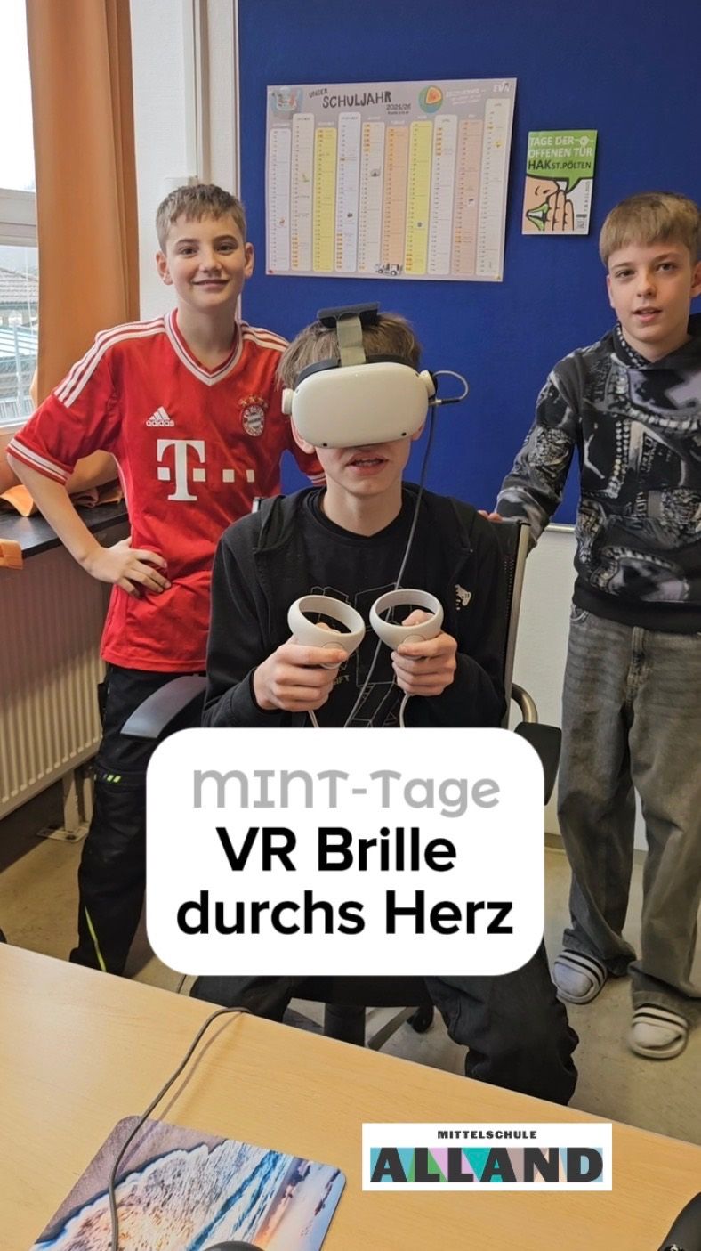 Three boys are playing a VR game. The boy in the middle wears a VR headset and holds controllers. The boy on the right smiles and leans on the chair. The boy on the left wears a red shirt.