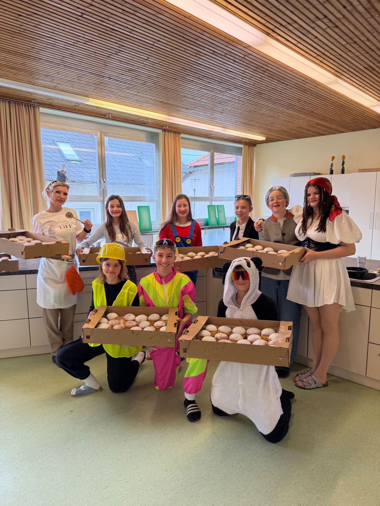 Eine Gruppe von Menschen in Kostümen posiert für ein Foto in einer Küche und hält Kartons mit Donuts.