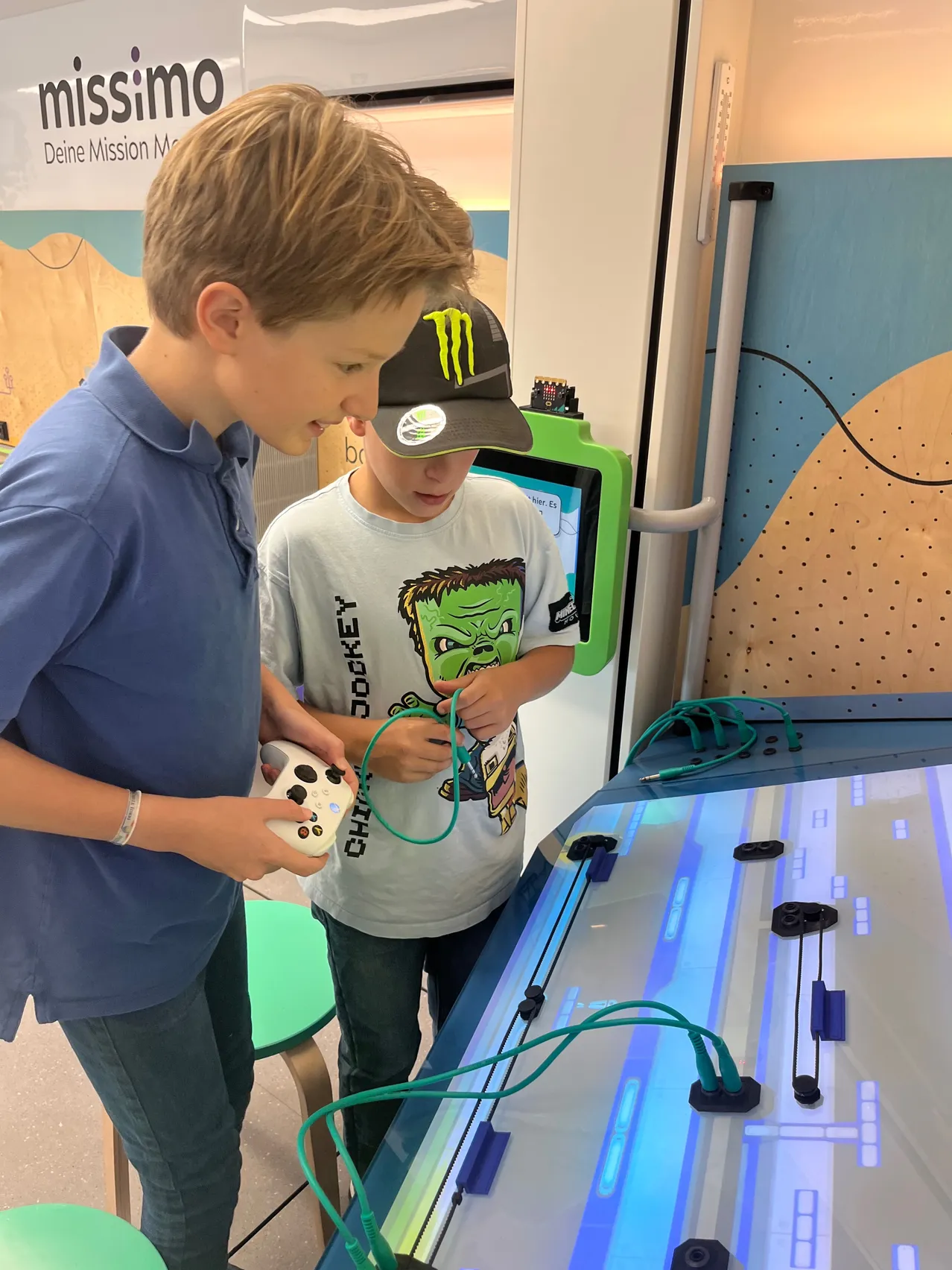 Zwei Jungen spielen ein Spiel auf einem großen Bildschirm, einer hält einen Spielcontroller.
