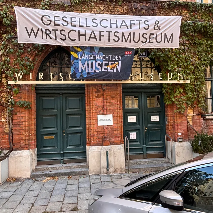 Ein Backsteingebäude mit grünen Türen und einem Banner, das Gesellschaft & Wirtschaftsmuseum besagt. Ein Auto ist davor geparkt.