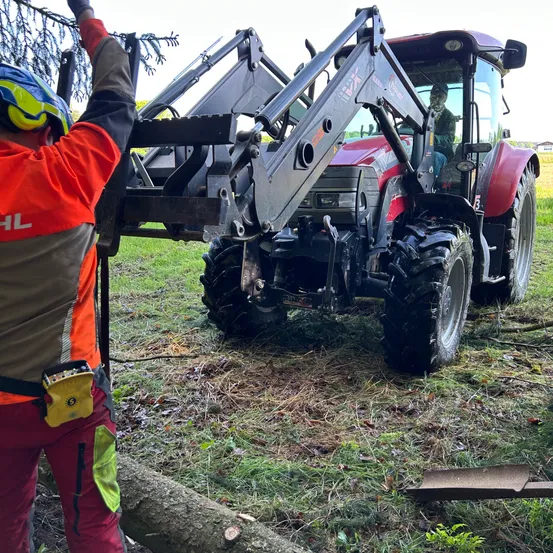 Ein Arbeiter in oranger Arbeitskleidung hält einen großen roten Traktor mit einem großen Metallaufsatz auf einem Rasen.
