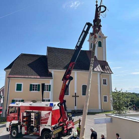 Ein Feuerwehrauto steht vor einer Kirche mit einem hohen Holzpfahl und einem Glockenturm.