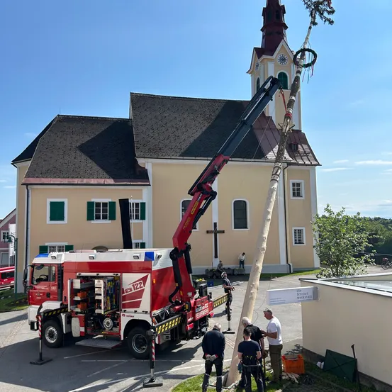Ein roter und weißer Kran mit Verlängerung steht neben einem Kirchengebäude, mit Leuten darum herum.