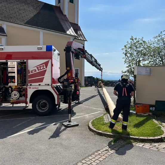 Ein Feuerwehrauto mit der Nummer 122 ist am Straßenrand geparkt. Ein Feuerwehrmann steht neben dem Fahrzeug, und eine weitere Person steht neben einem Baum.
