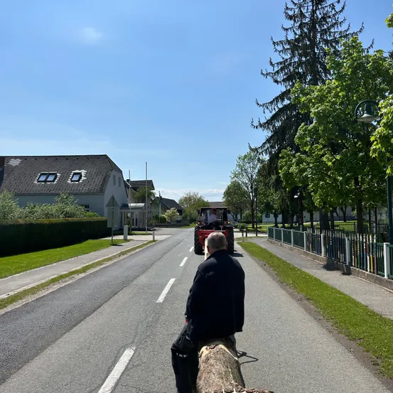 Ein Mann sitzt auf einem Baumstamm in der Mitte der Straße und beobachtet, wie ein Traktor vorbeifährt.