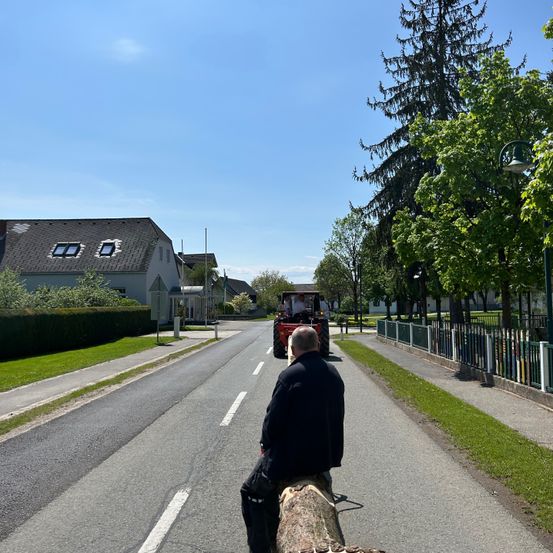Ein Mann sitzt auf einem Baumstamm in der Mitte der Straße und beobachtet, wie ein Traktor vorbeifährt.