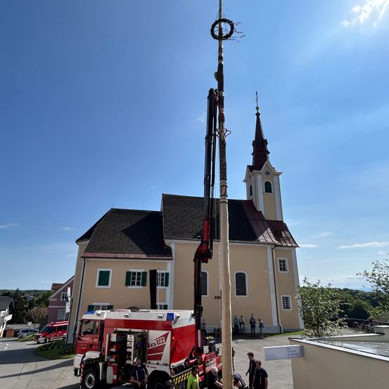 Ein Feuerwehrauto steht an einem sonnigen Tag vor einer Kirche. Ein Mann steht im Inneren des Fahrzeugs.