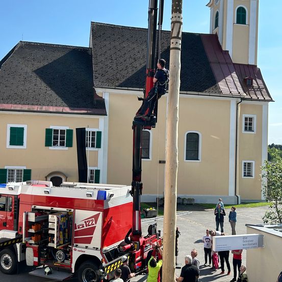 Ein Mann klettert an einem Mast mit Hilfe eines Feuerwehrwagens als Leiter in der Front einer Kirche.