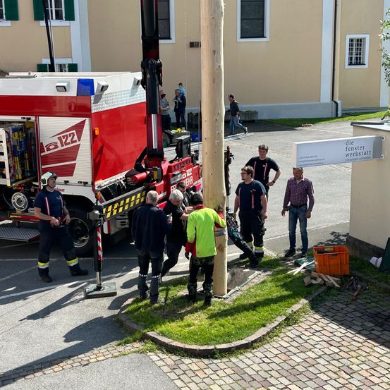 Eine Gruppe von Feuerwehrleuten arbeitet an einem Pfosten vor einem Gebäude. Sie tragen Uniformen, und einige von ihnen tragen Helme. Ein Feuerwehrwagen ist in der Nähe geparkt.