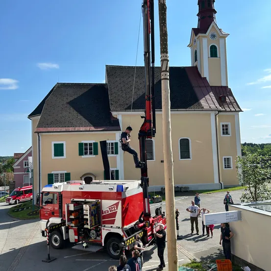 Ein Mann klettert mit einem Kran an einem Pfahl vor einer Kirche mit Turm hoch.
