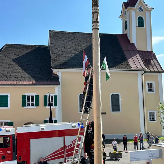 Ein Mann klettert auf eine Leiter zu einem Fahnenmast mit Flaggen vor einer Kirche.