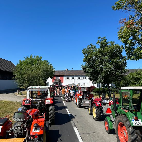 Traktoren, die am Straßenrand unter einem blauen Himmel geparkt sind, mit vorbeigehenden Menschen und Gebäuden im Hintergrund.