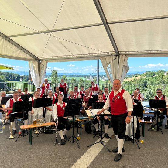 Eine Gruppe von Musikern in traditioneller Kleidung tritt unter einem Zelt mit malerischer Bergkulisse im Hintergrund auf.