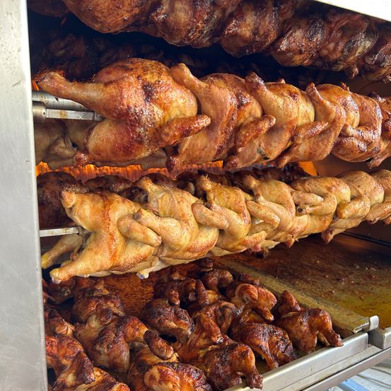 Mehrere Hühner werden in einem kommerziellen Ofen gekocht, an Haken hängend, mit knuspriger Haut und goldbrauner Farbe.