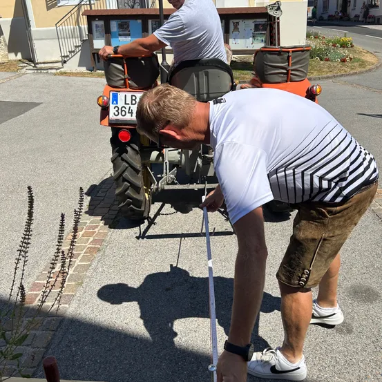Ein Mann beugt sich vor, um die Vorderseite eines Traktors mit dem Kennzeichen LB 364 zu justieren, während ein anderer Mann auf dem Fahrersitz sitzt.
