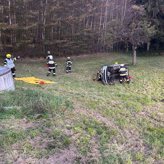 Rettungskräfte sind am Unfallort. Ein Auto ist in einem Grasfeld umgekippt. Die Besatzung ist in voller Ausrüstung.