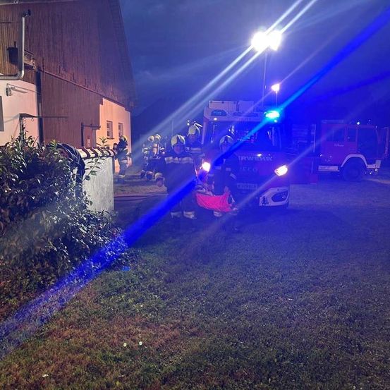 Feuerwehrleute sind bei Nacht vor Ort und helfen einer Person in einem roten Stuhl mit einem Feuerwehrwagen in der Nähe.