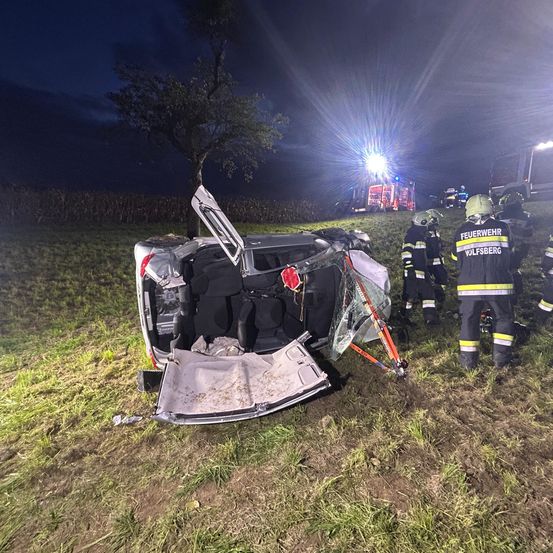 In der Nacht ereignete sich auf einem Grasfeld ein Autounfall, an dem Feuerwehrleute und Rettungsfahrzeuge beteiligt waren. Das Auto ist umgekippt und die Türen sind offen.