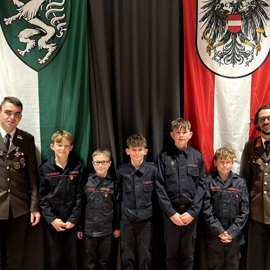 Eine Gruppe junger Jungen in Uniformen mit militärischen Abzeichen posiert für ein Foto vor Flaggen.