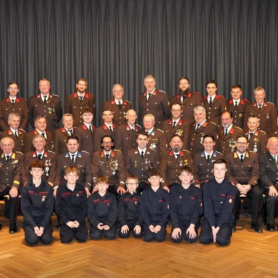 Eine große Gruppe uniformierter Personen, einschließlich Offiziere und Kadetten, posiert für ein Foto. Die Offiziere sitzen hinten, während die Kadetten vorne knien. Sie tragen alle Medaillen und Brillen.