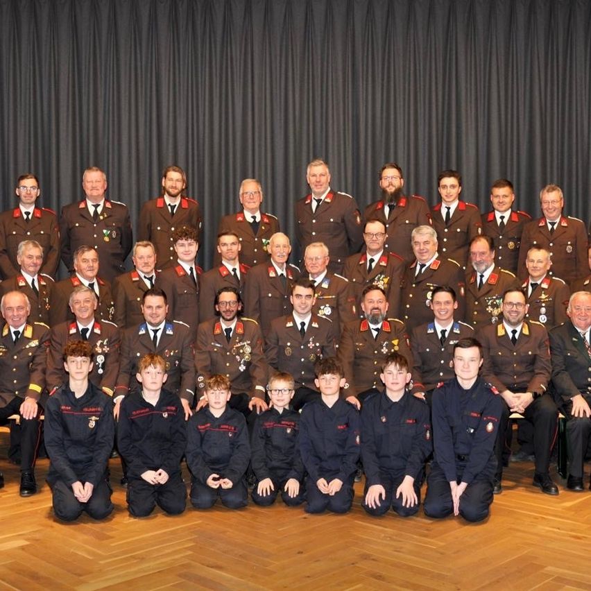 Eine große Gruppe uniformierter Personen, einschließlich Offiziere und Kadetten, posiert für ein Foto. Die Offiziere sitzen hinten, während die Kadetten vorne knien. Sie tragen alle Medaillen und Brillen.